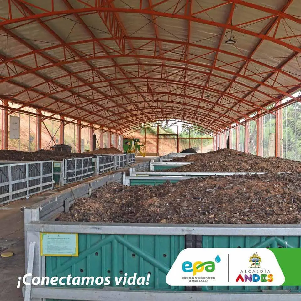 Interior de una planta de compostaje con operarios y pilas de compost bajo cubierta metálica